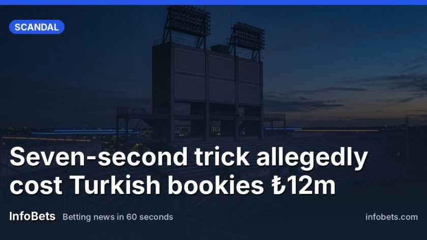 A tall, unlit stadium tower stands against a dusk sky, its blank rectangular panels dark and smooth, with floodlight rigs silhouetted above and empty tiered seats stretching quietly beneath in soft…